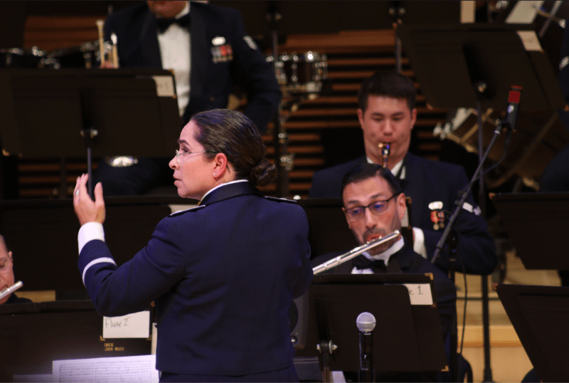 a photo of the conductor of the Band of the Golden West with her arms up, looking sideways