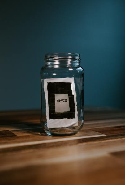 A glass jar with a polaroid photo inside. The polaroid photo is of a white paper against black tiles with "memories" written on it.