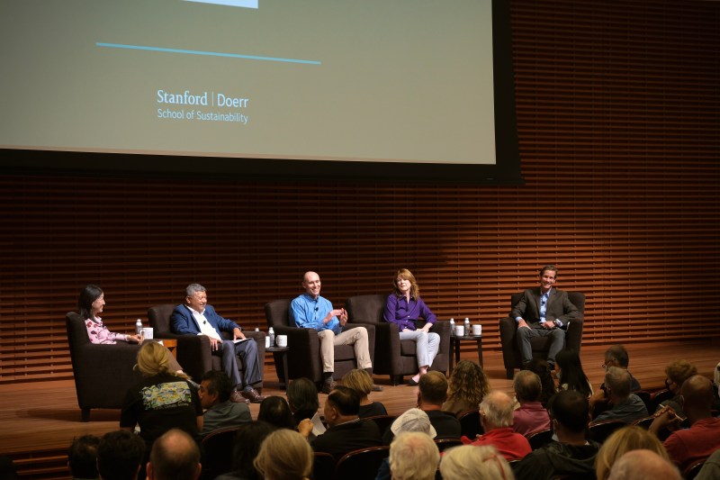 Left sideview Five panelists sitting in a row on stage with audience in foreground.