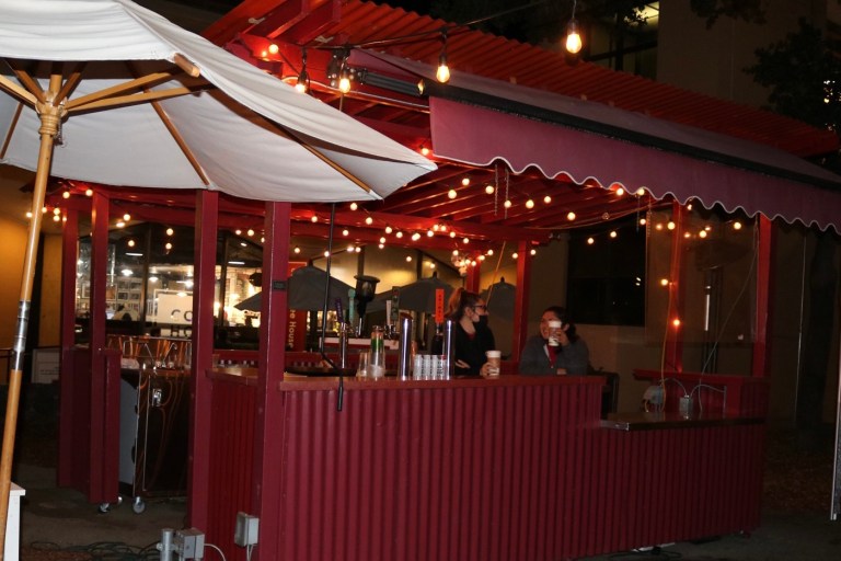 Two people holding disposable coffee cups stand near a red booth set up at Tressider Memorial Union.