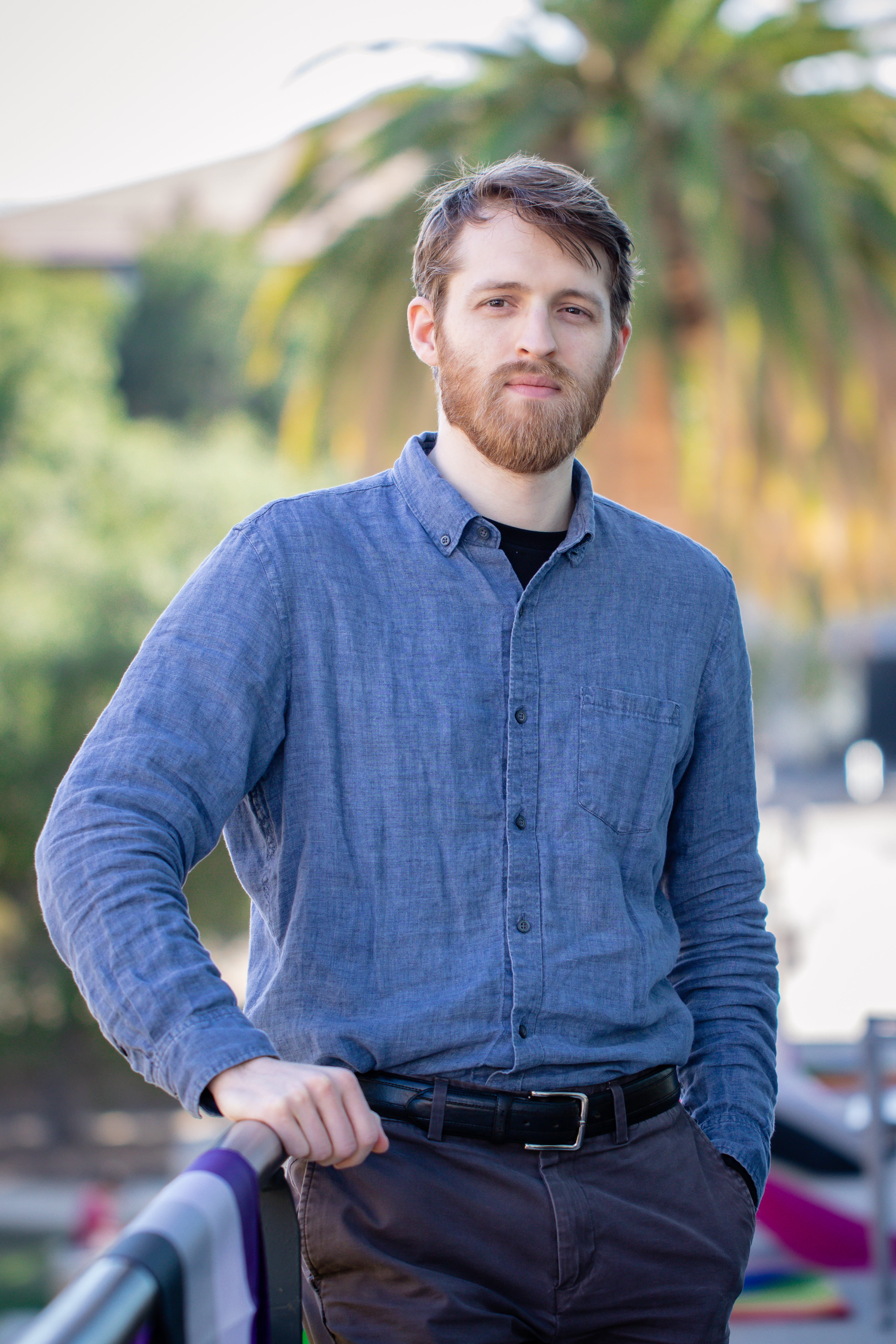 Andrew Beel leans against a railing with a palm tree in the background.