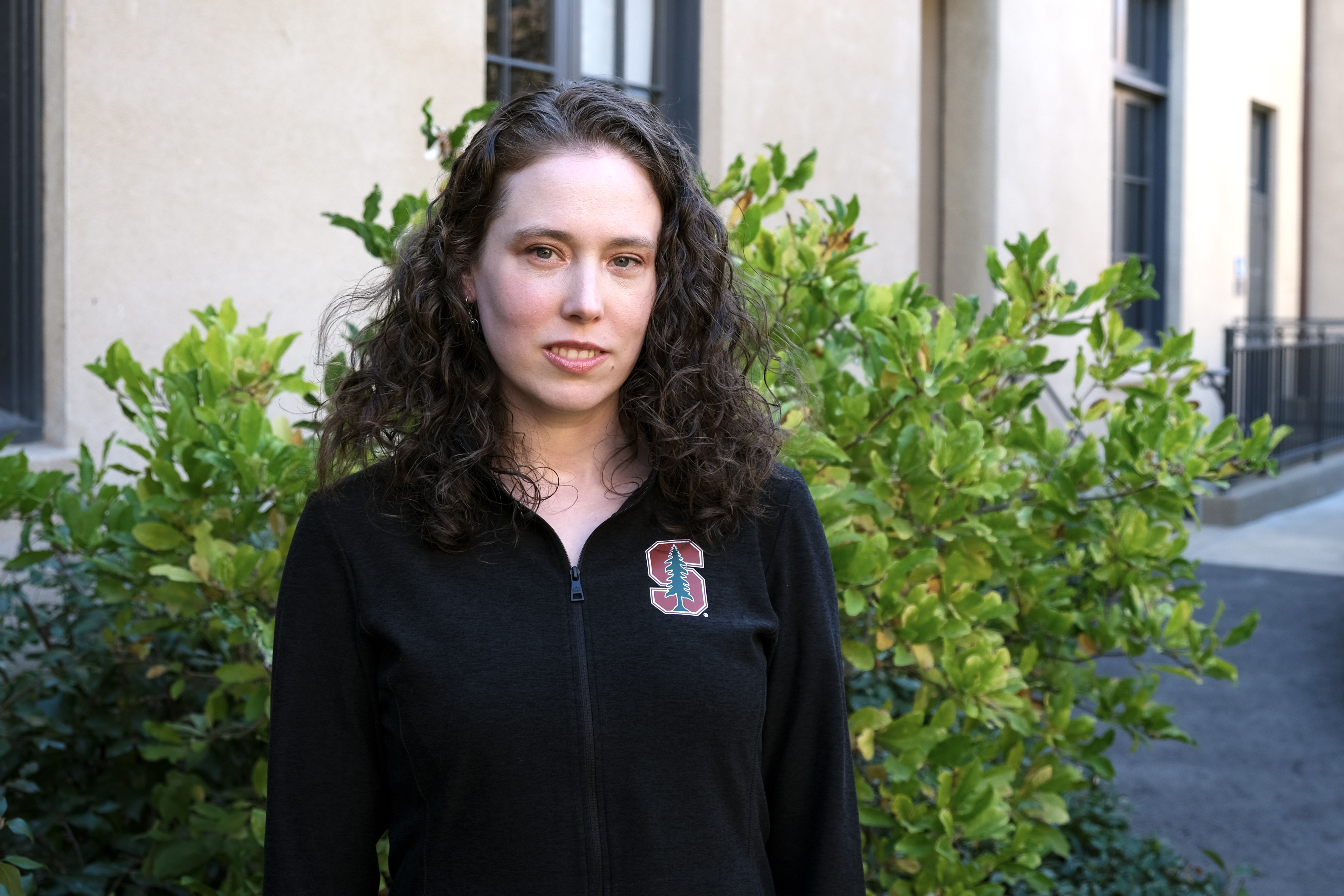 Sherri Rose stands in front of a green bush outside a tan building.