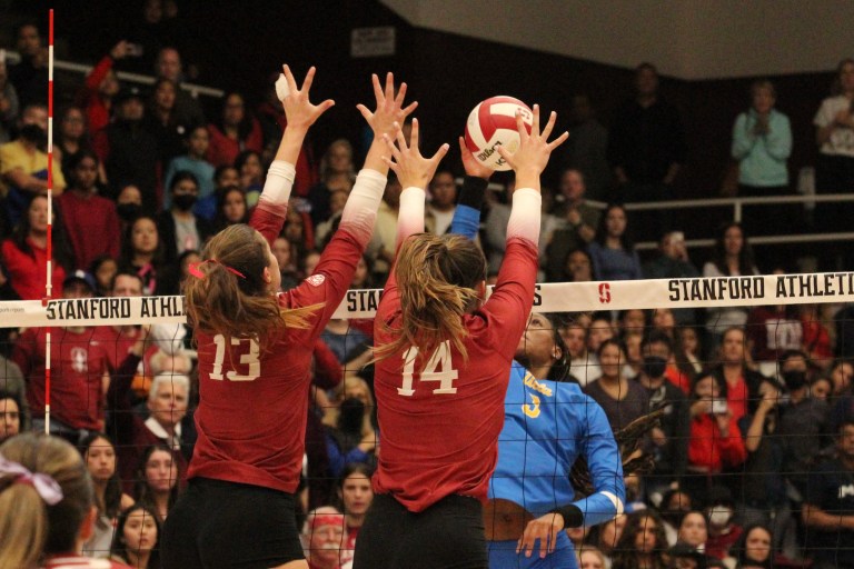 Two volleyball players jump up to block the ball