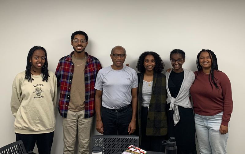 Biratu and students standing in front of a while wall.