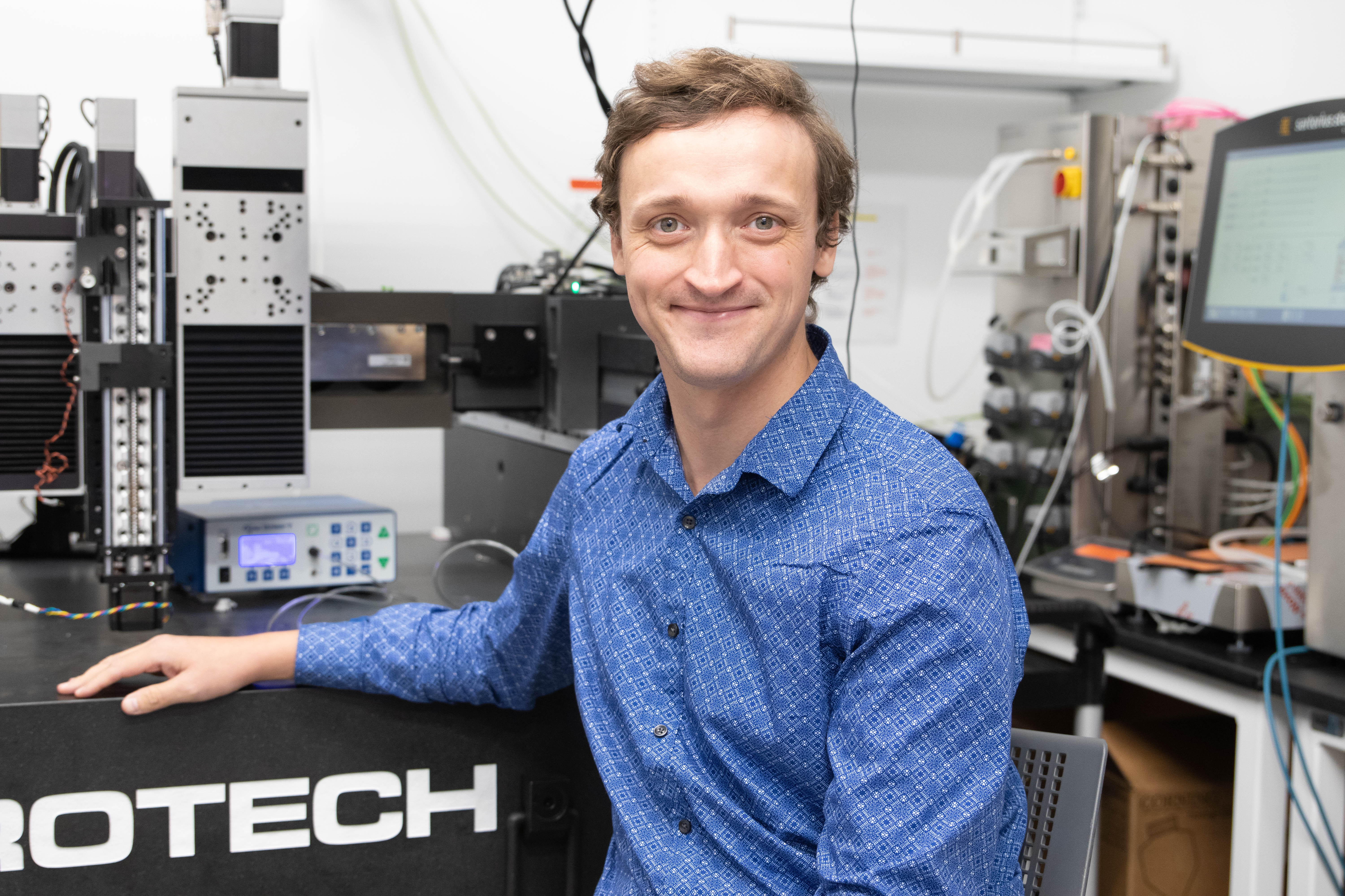 Mark Skylar-Scott​ sits with equipment for a portrait while wearing a blue collared shirt.