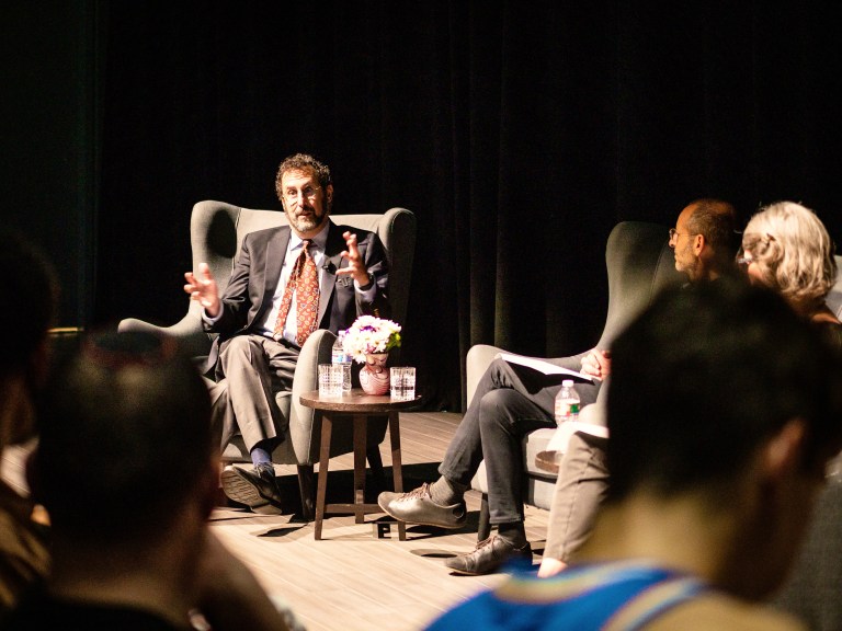 A photo of playwright Tony Kushner sitting under the spotlight talking and gesturing emphatically.