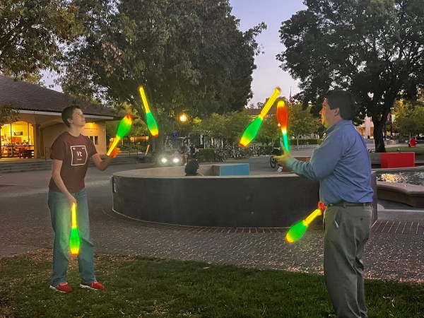 Two juggling club members stand on the White Plaza lawn, each juggling three neon clubs.