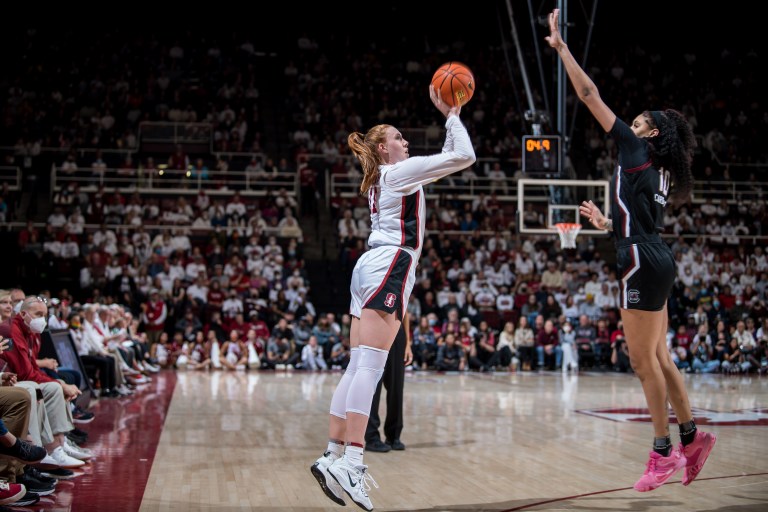 A basketball player rises up to shoot a jumpshot with a defender contesting