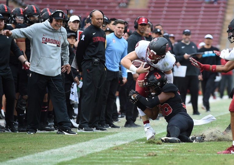 A football player tackles the opponent in front of his sideline with the team watching