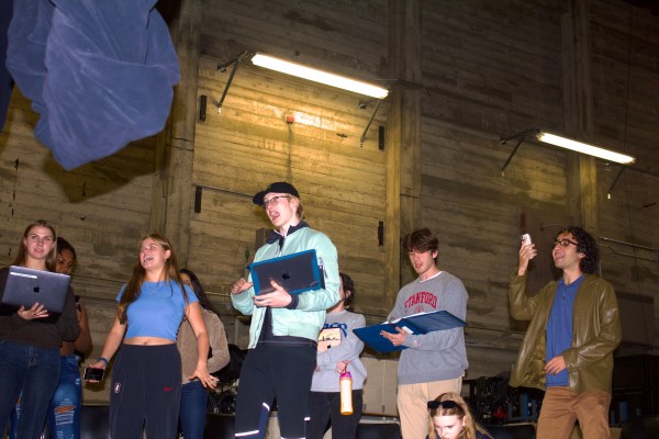 Nine people sing together standing up, with their phones, laptops or scripts in their hands