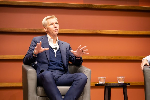 Harry Brekelmans sits in a grey chair on stage, water to his left, with an orange background.