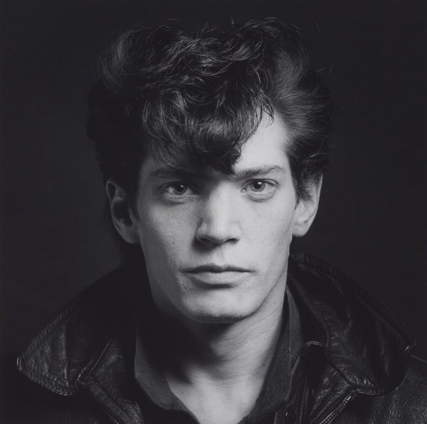 The black and white headshot of a man staring into the camera, with bangs covering his forehead