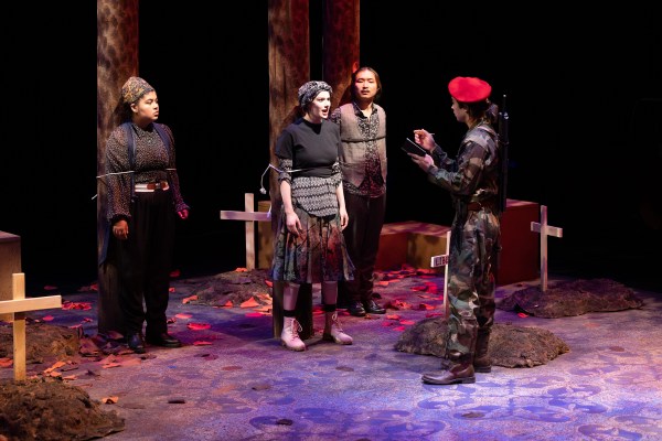 Three people are being tied to posts, while a soldier wearing camouflage and a red cap is taking notes of what they are saying.