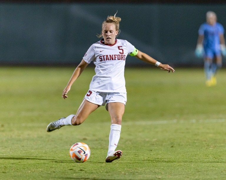 A female soccer player in a white uniform prepares to kick the ball