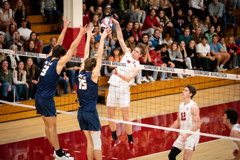 A volleyball player jumps at the net with two defenders closeby