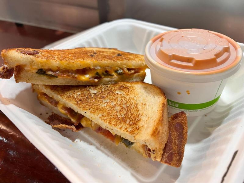 Two grilled cheese with obscure fillings and tomato soup in a to-go cup.