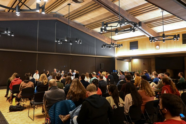 A crowd of 100 or so people sit in a high-ceiling room.