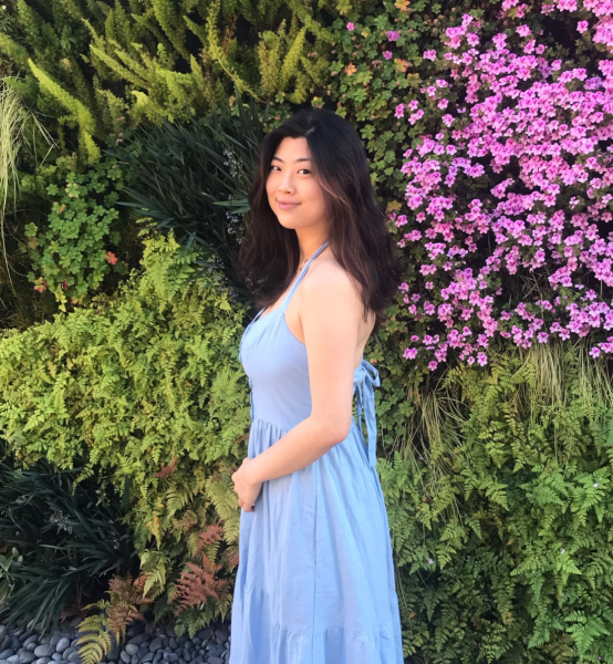 Girl wearing blue dress standing in front of green and floral background.