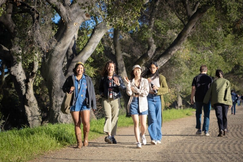 Four students smile and wave as they walk on the trail.