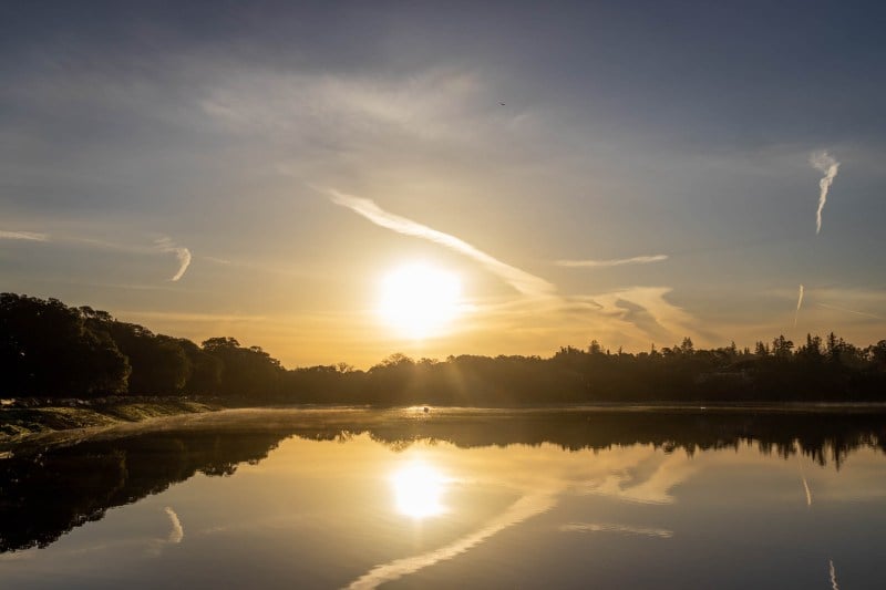 Landscape of the lake with the sun in the sky reflected on the water to create a symmetric image.