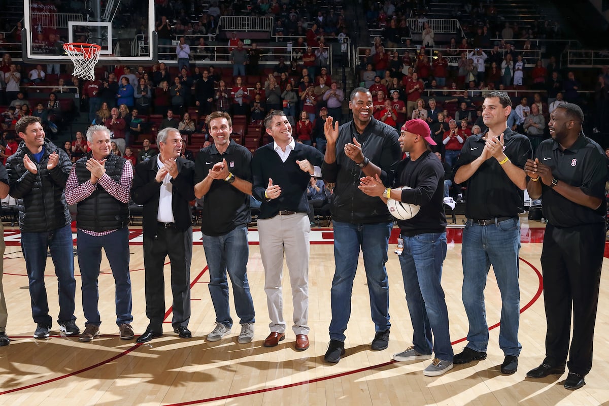 A group of men stand on a basketball court clapping.