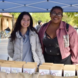 Two women stand behind a display of dried fruits.