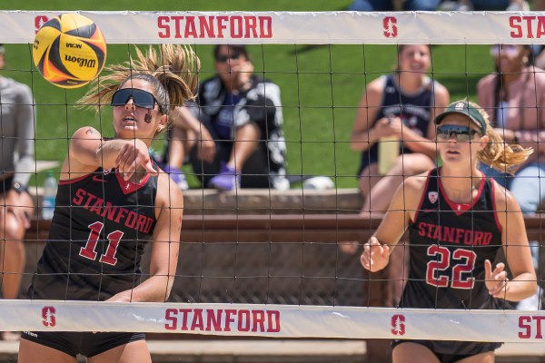 Maddi Kriz hits the ball during a beach volleyball match, while Charlie Ekstrom looks on through the net.