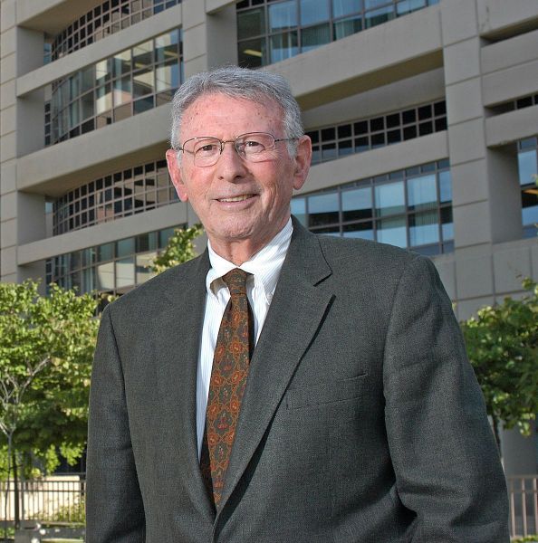 A man in a suit in front of trees.