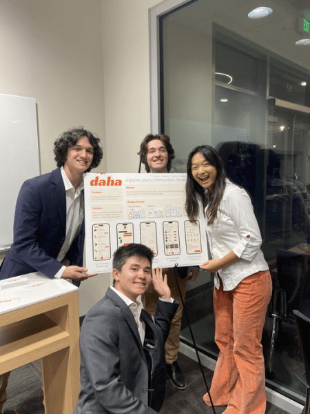 Four students pose with a poster stand titled "daha."