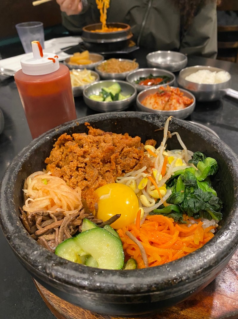 Pork, egg yolk, sprouts, greens and carrots simmer in a stone bowl.