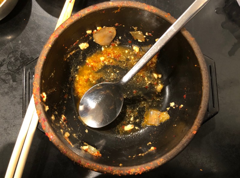 A stone bowl with a spoon in it contains remnants of tofu soup.