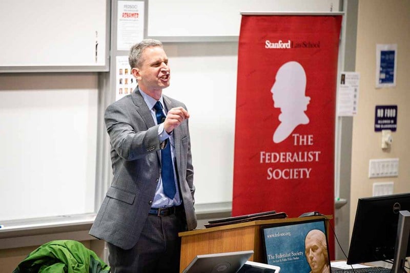 A man talking in front of a red banner.