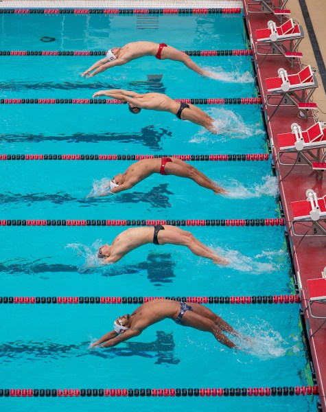 5 swimmers dive into a pool at the same time face up.