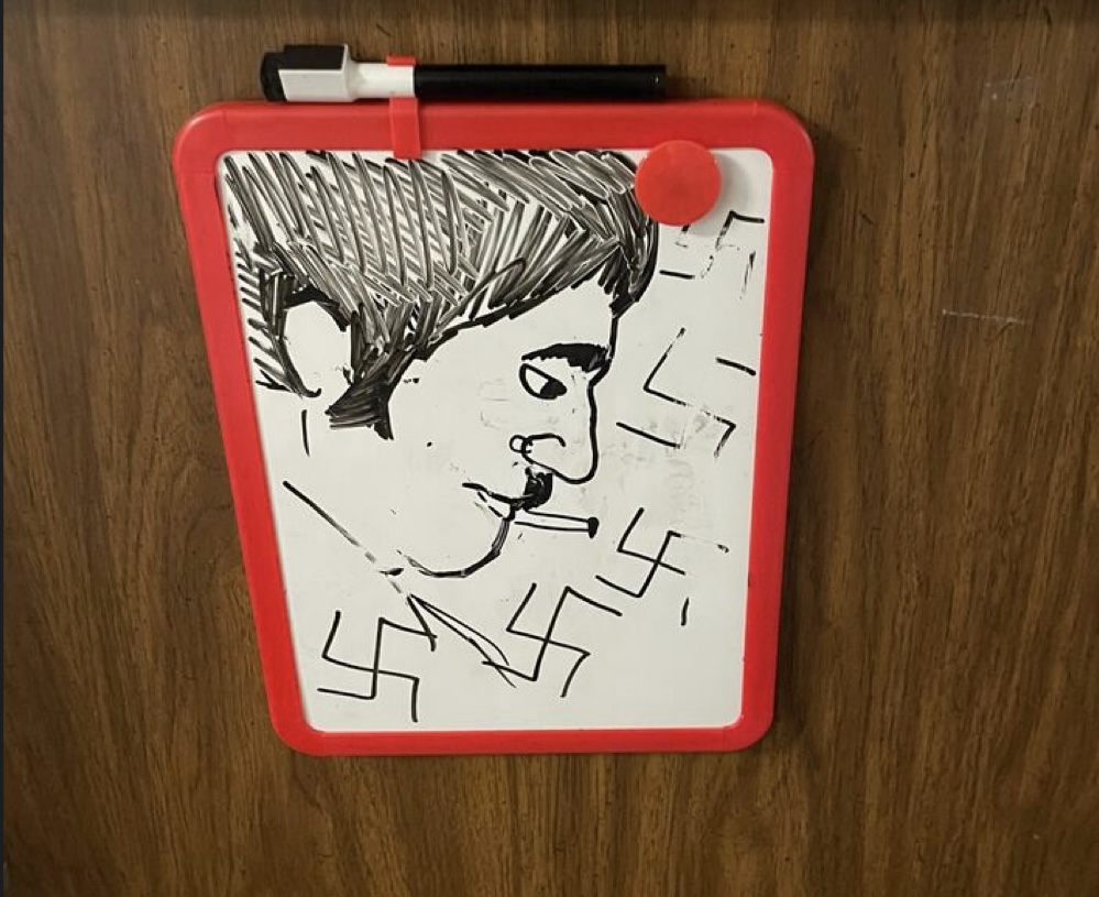 A drawing of a person resembling Hitler surrounded by swastikas on a whiteboard attached to a door