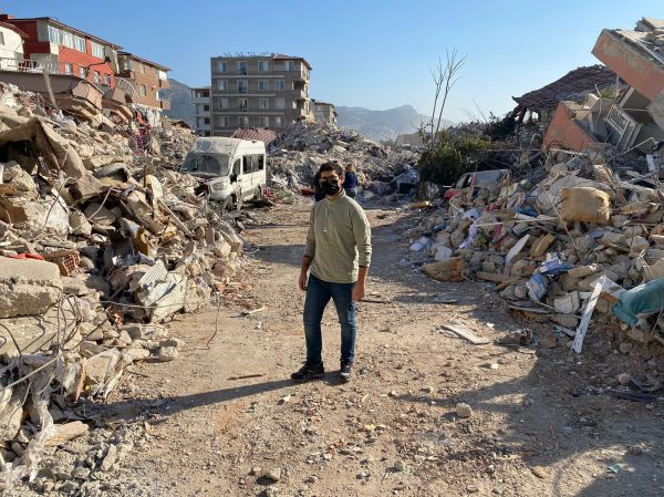 A man stands in the middle of a road with ruins on either side of him