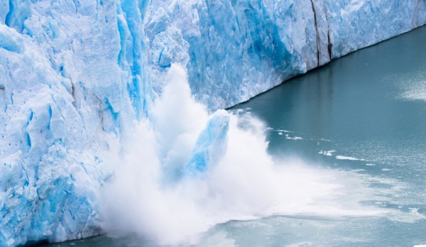 Collapsing ice glacier, large chunks of blue ice falling in the sea, making a splash.