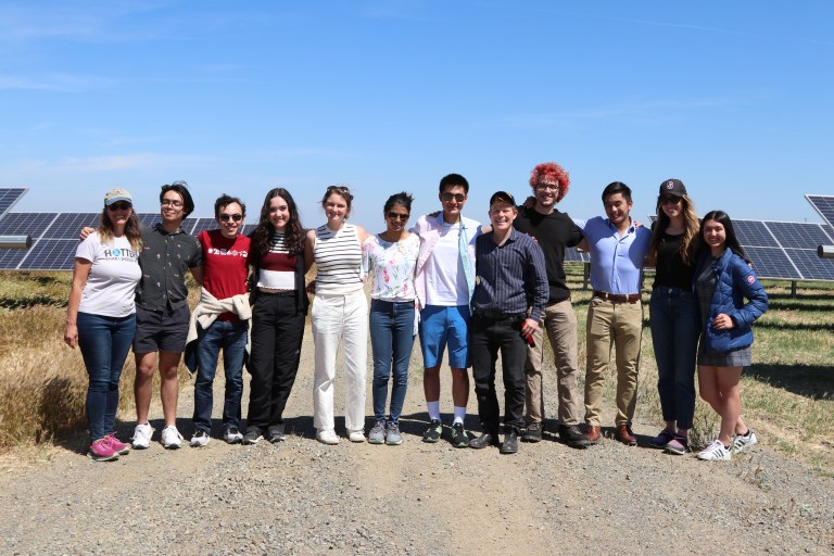 Twelve people pose in front of the Lemoore Solar Farm on a sunny afternoon.