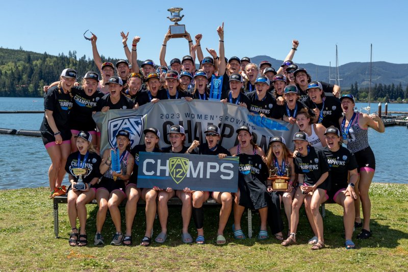 The Stanford Rowers team celebrates on the waterfront with a sign that says "PAC 12 CHAMPS"