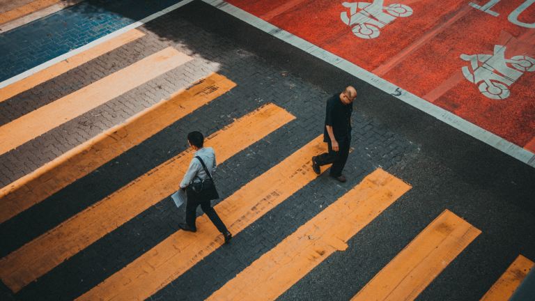 Two people walk past each other on a yellow crosswalk.