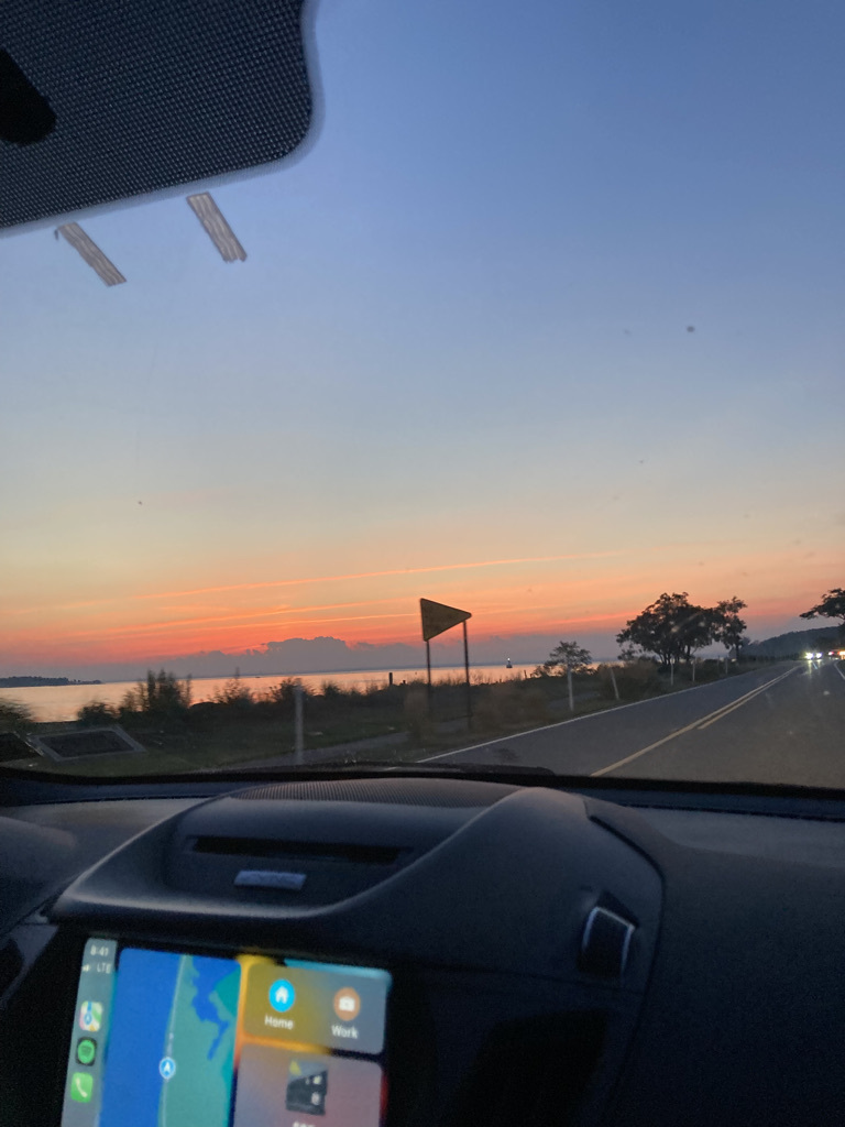 Looking out from inside a car. Driving down the coast. The sun is setting in the distance.