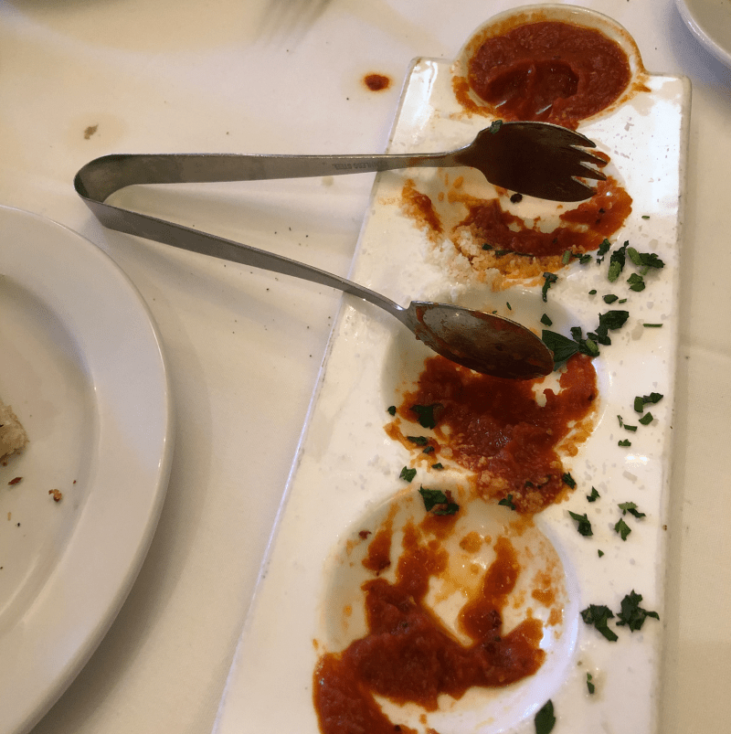 The finished arancine dish sits on a white table cloth with tongs and leftover sauce in it. 