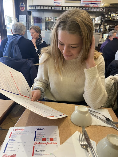 A student sits across a small cafe table. She is reading a menu. 