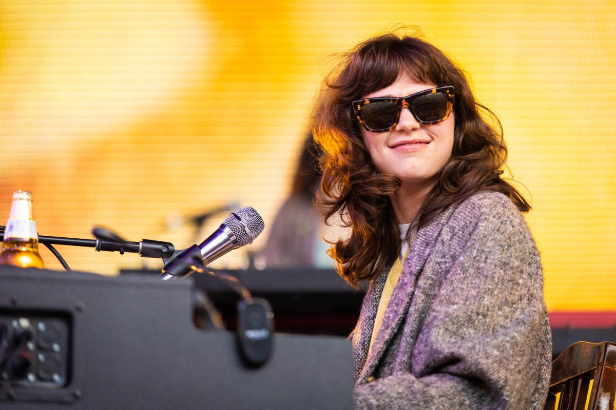 a photo of a smiling person with light skin and medium-length wavy brown hair, sitting at a piano and smiling