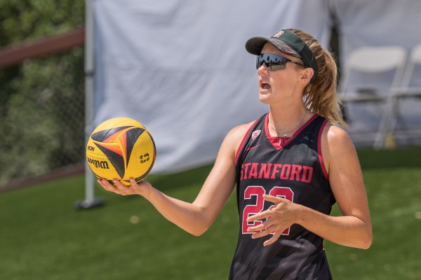 Charlie Ekstrom prepares to serve a black and yellow ball during a beach volleyball match.