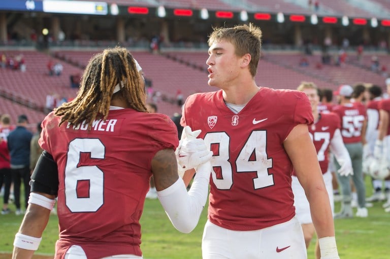 Two players in uniform on a football field. One's back is turned to the camera.