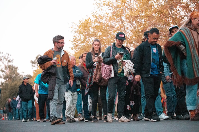 Dozens of people ranging in age, some dressed in tie dye and fringe, wait in line. 