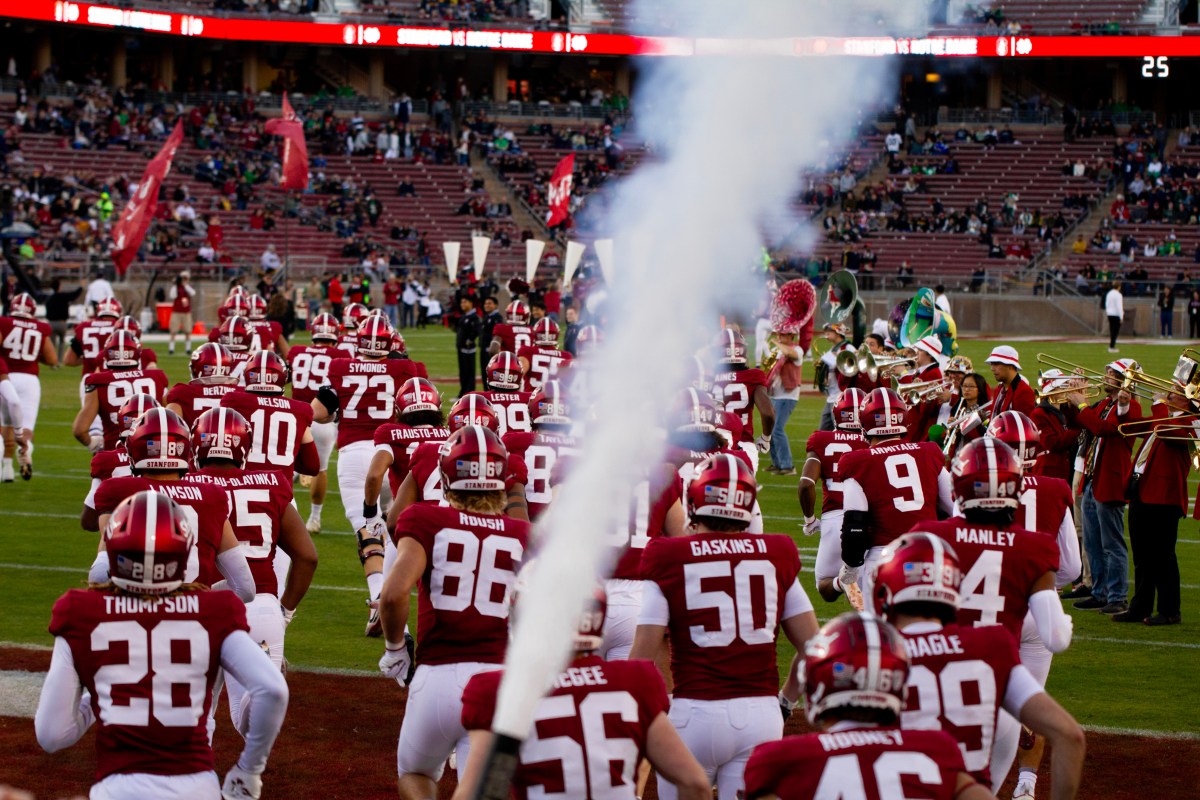 Stanford players run onto the field while a steam cannon fires. Marching band players play on the field.