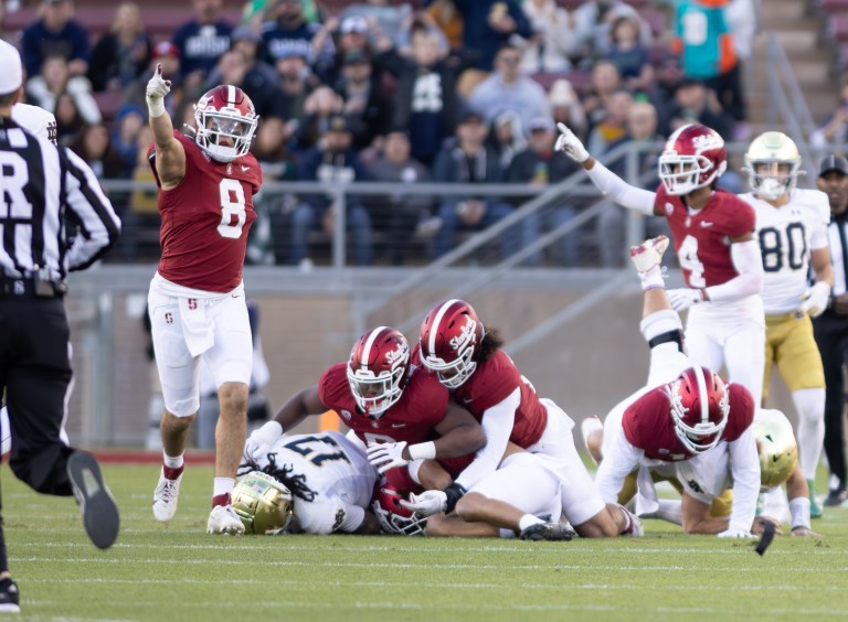 Stanford players point toward the Notre Dame end zone, indicating a turnover. Two others tackle a Notre Dame player.