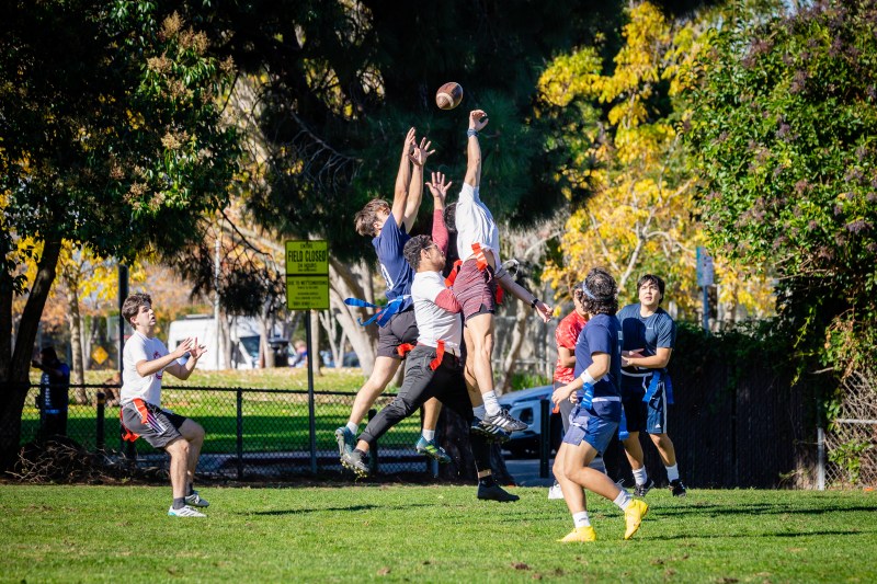 Flag football players leap in the air to catch a football.