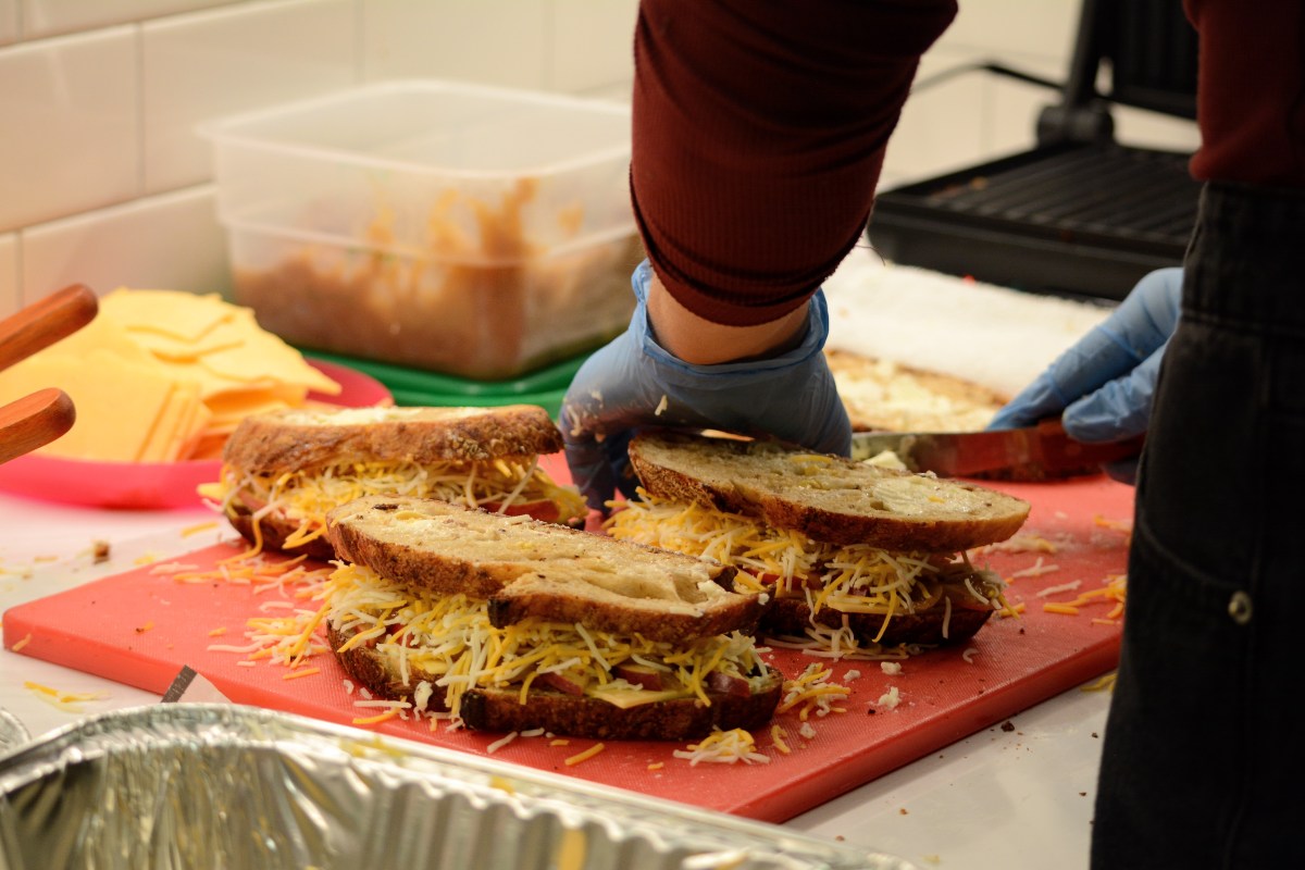 A person wearing blue gloves makes a sandwich. 